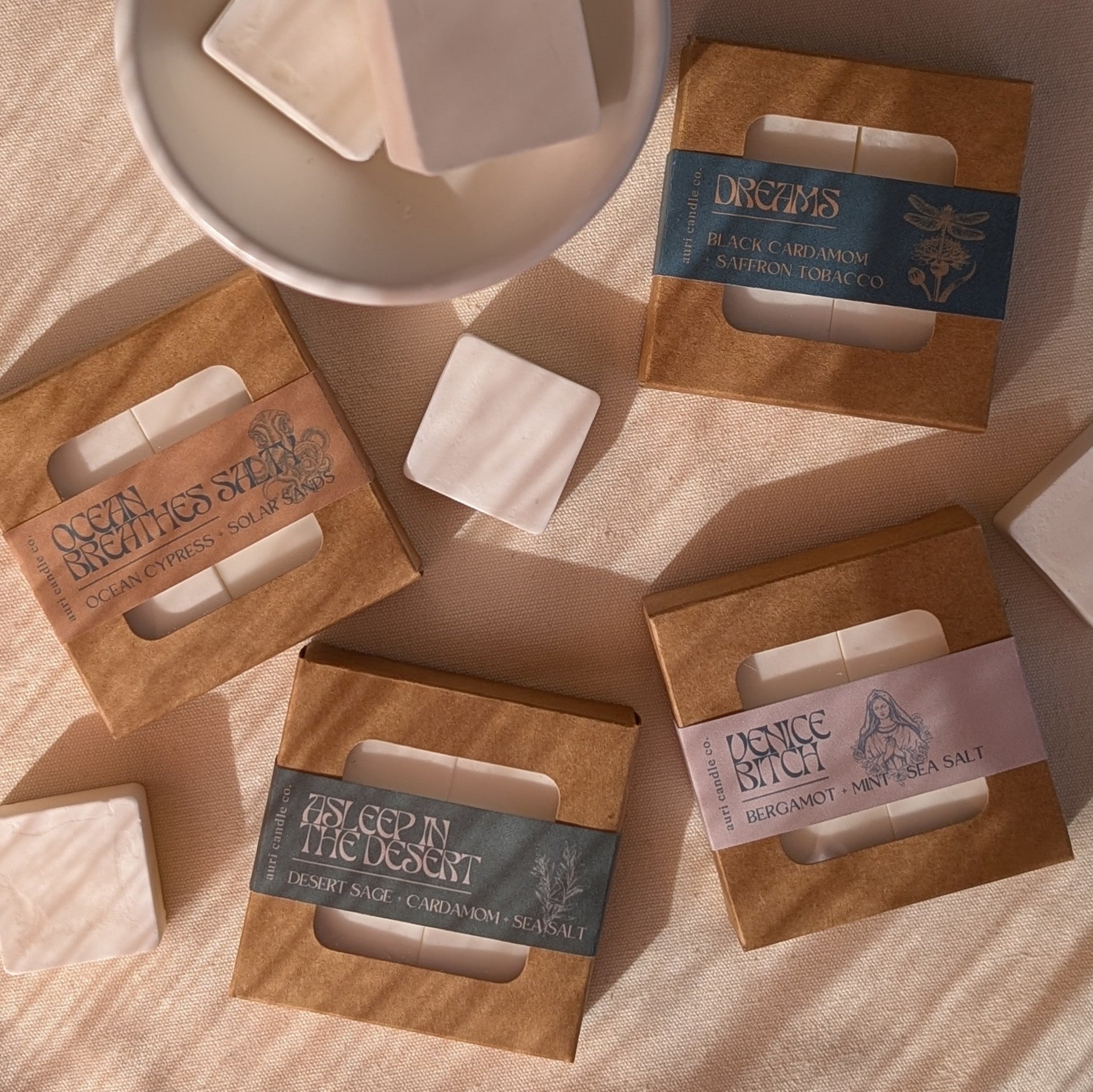 A wax warmer and four candle scent samplers with labels, arranged on a surface with a bowl in the background.