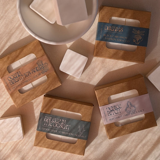 A wax warmer and four candle scent samplers with labels, arranged on a surface with a bowl in the background.